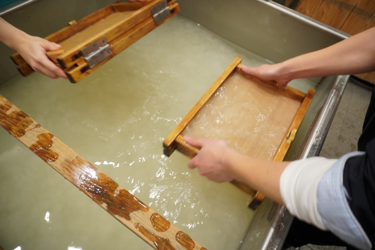 流し漉きの工程の一部。原料が混ざった水を深く汲み繊維を絡ませる